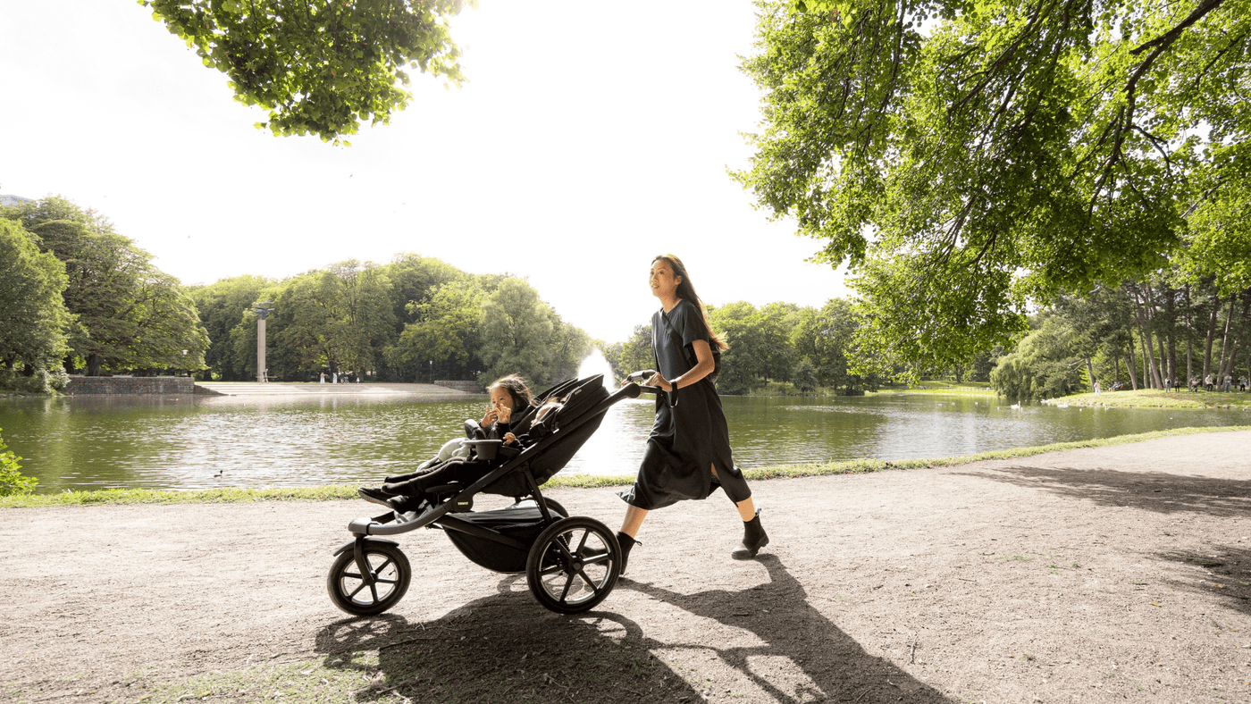 Woman walking by a pretty lake with the Thule Urban Glide 3 jogging stroller